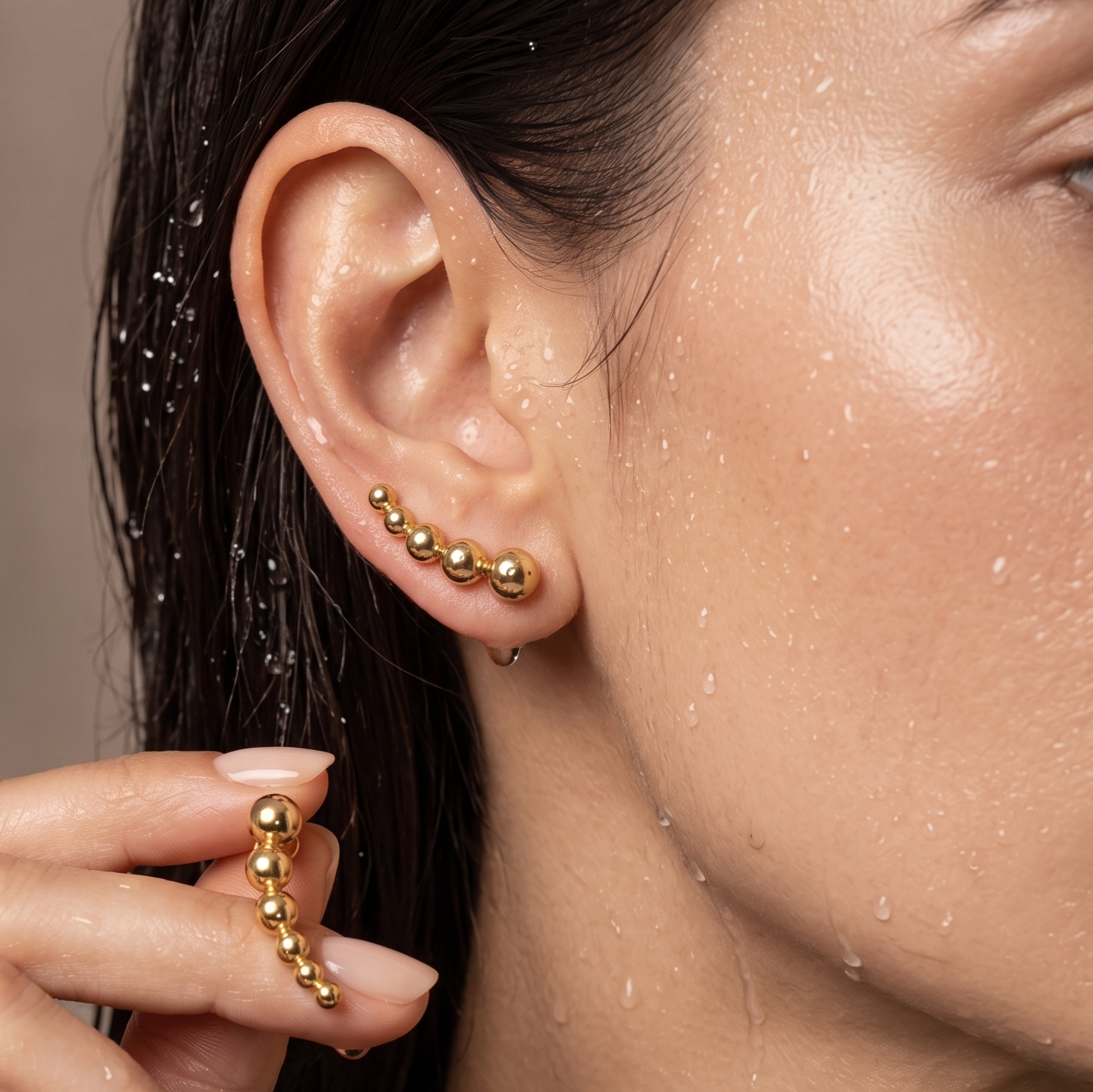 Bibi Studs graduated gold ball stud earrings worn and held by wet model – hypoallergenic non-tarnish waterproof stainless steel everyday gold stud earrings