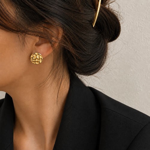 Chrysa Studs textured circular gold disc stud earrings with hammered cobblestone surface on a lightskinned model – hypoallergenic 316L stainless steel, tarnish-free and nickel-free for everyday and going-out wear