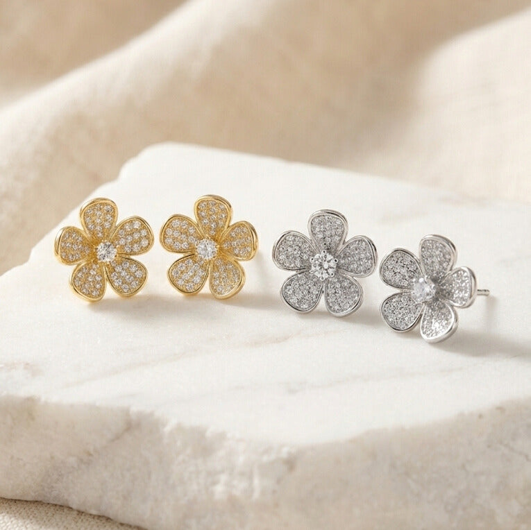 Daeze Studs pavé CZ stud earrings in gold and silver with cubic zirconia flower petals and solitaire centre on white stone surface – surgical steel water resistant sparkle earrings