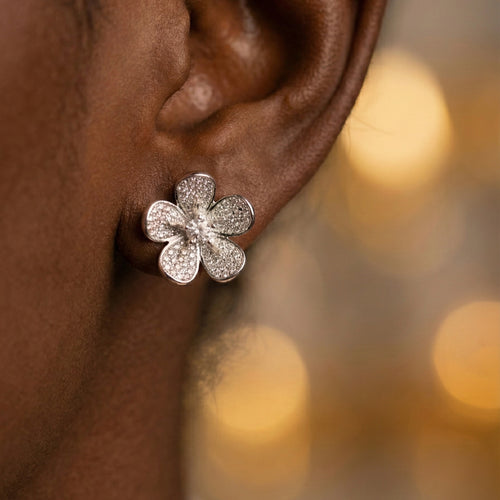 Daeze Studs silver pavé CZ flower stud earrings with cubic zirconia petals and solitaire centre worn by model against golden bokeh background – surgical steel sparkle earrings for sensitive ears