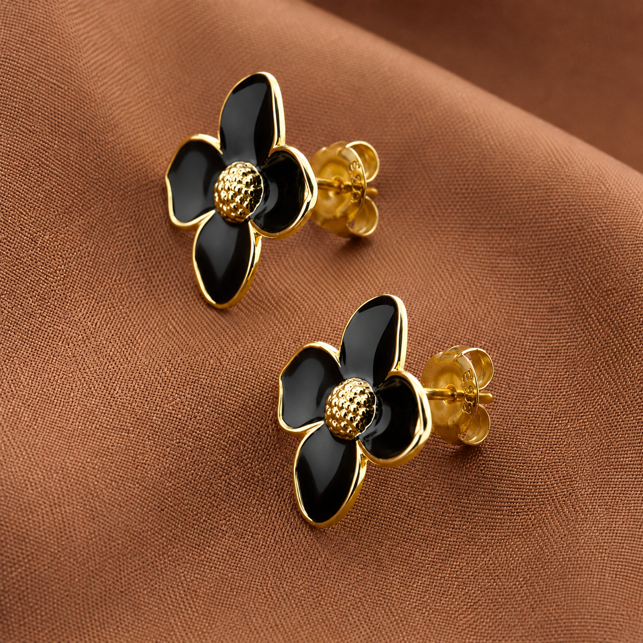 Dalia Studs black and gold enamel floral stud earrings with four petals and textured gold centre on warm fabric – hypoallergenic nickel-free stainless steel earrings