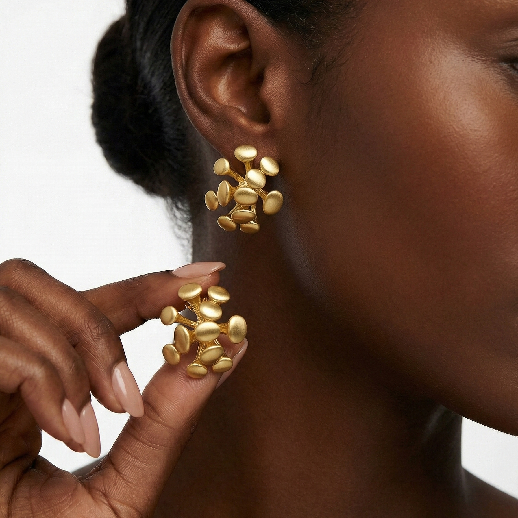 Dugo Studs brushed gold petal cluster earrings worn and held by model with radiating oval petal design – hypoallergenic stainless steel statement earrings for sensitive ears