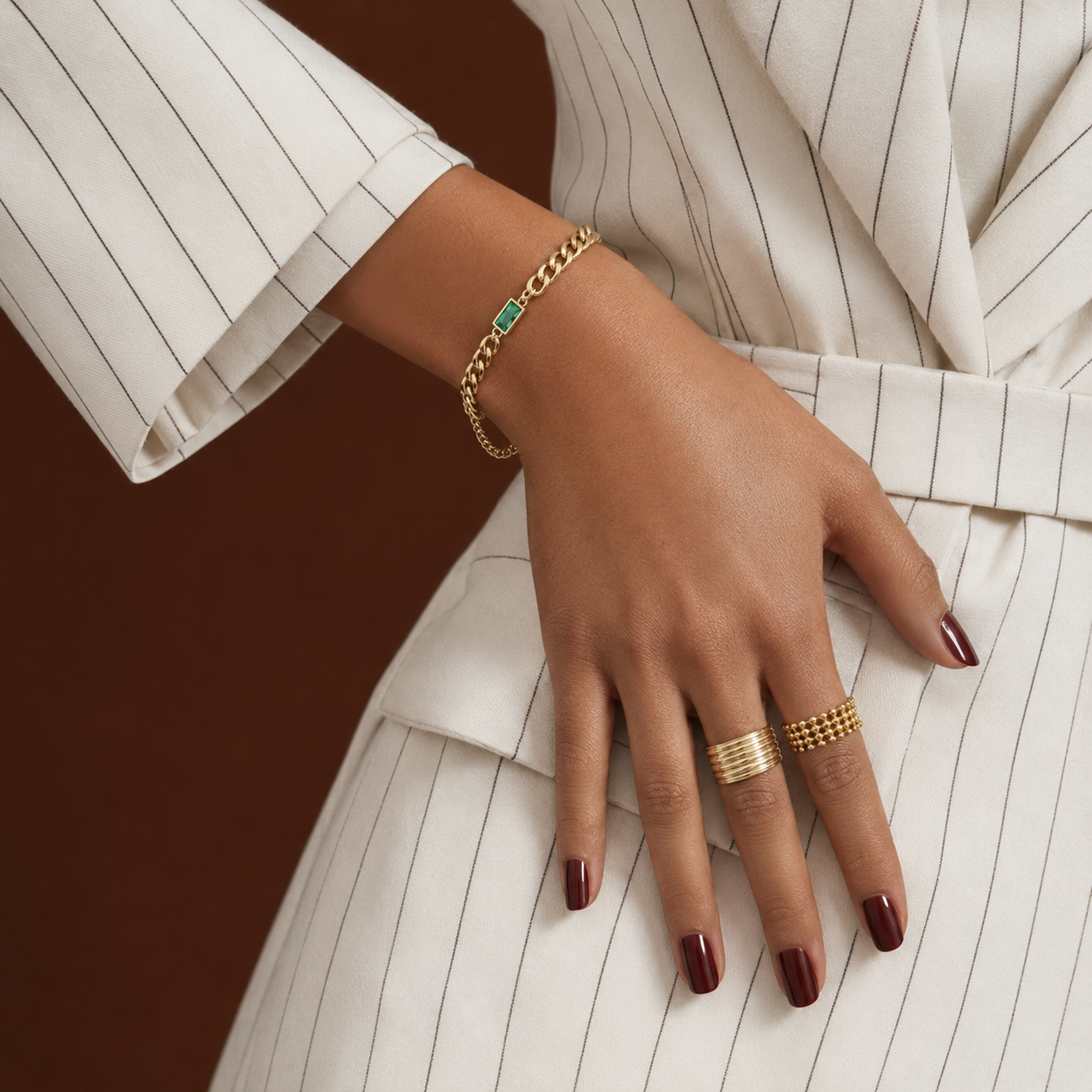 Esme Bracelet gold curb chain bracelet with green baguette CZ stone worn on wrist with pinstripe blazer – waterproof non-tarnish hypoallergenic stainless steel women's bracelet