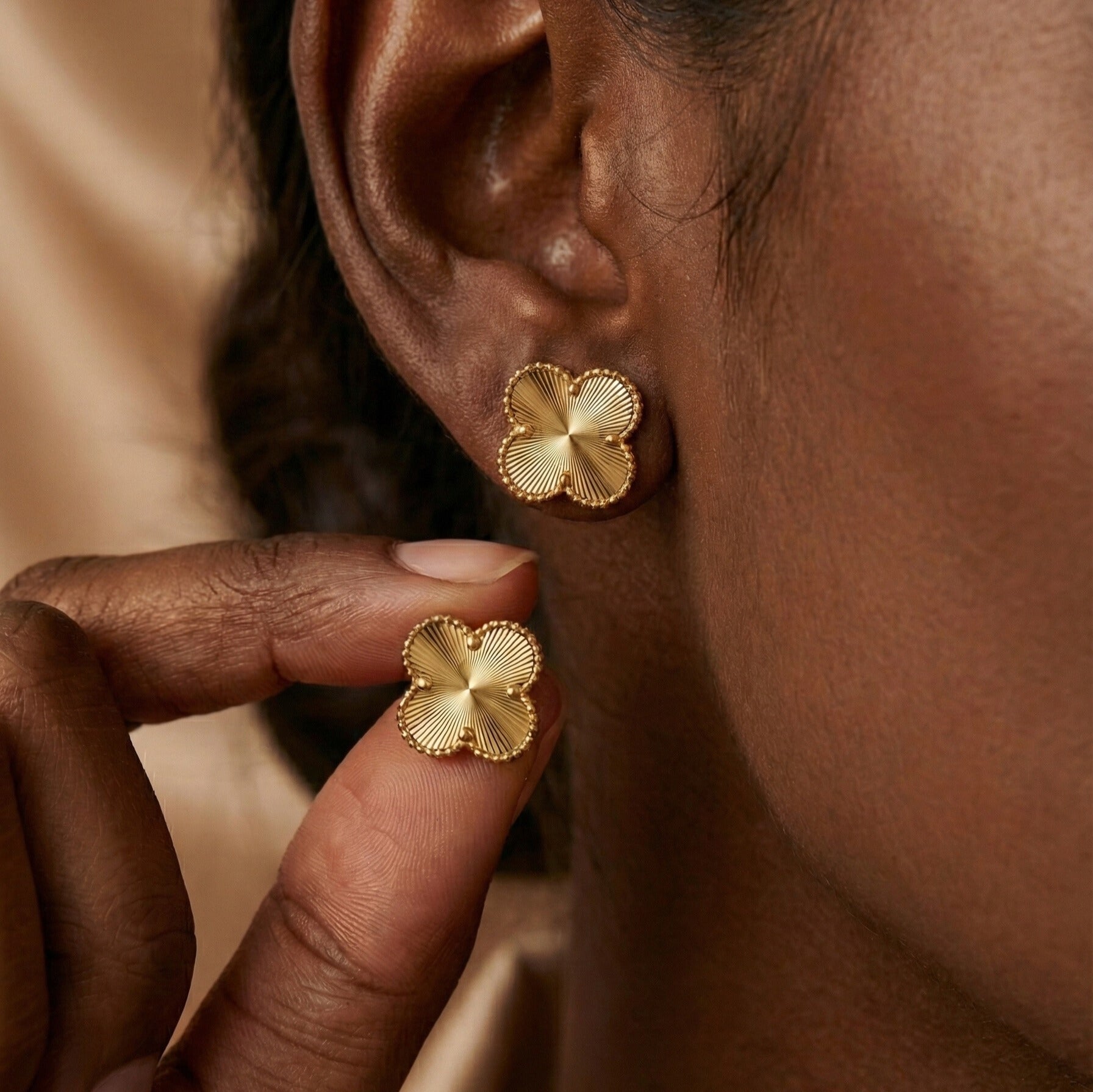 Eva Studs gold clover stud earrings with radiating sunburst engraving worn and held by model – tarnish-free waterproof hypoallergenic stainless steel four leaf clover stud earrings for sensitive ears