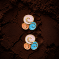 Kima Studs colourful enamel swirl stud earrings in pink, coral and blue with gold spiral detail on dark textured background – hypoallergenic statement stud earrings, tarnish-free surgical steel