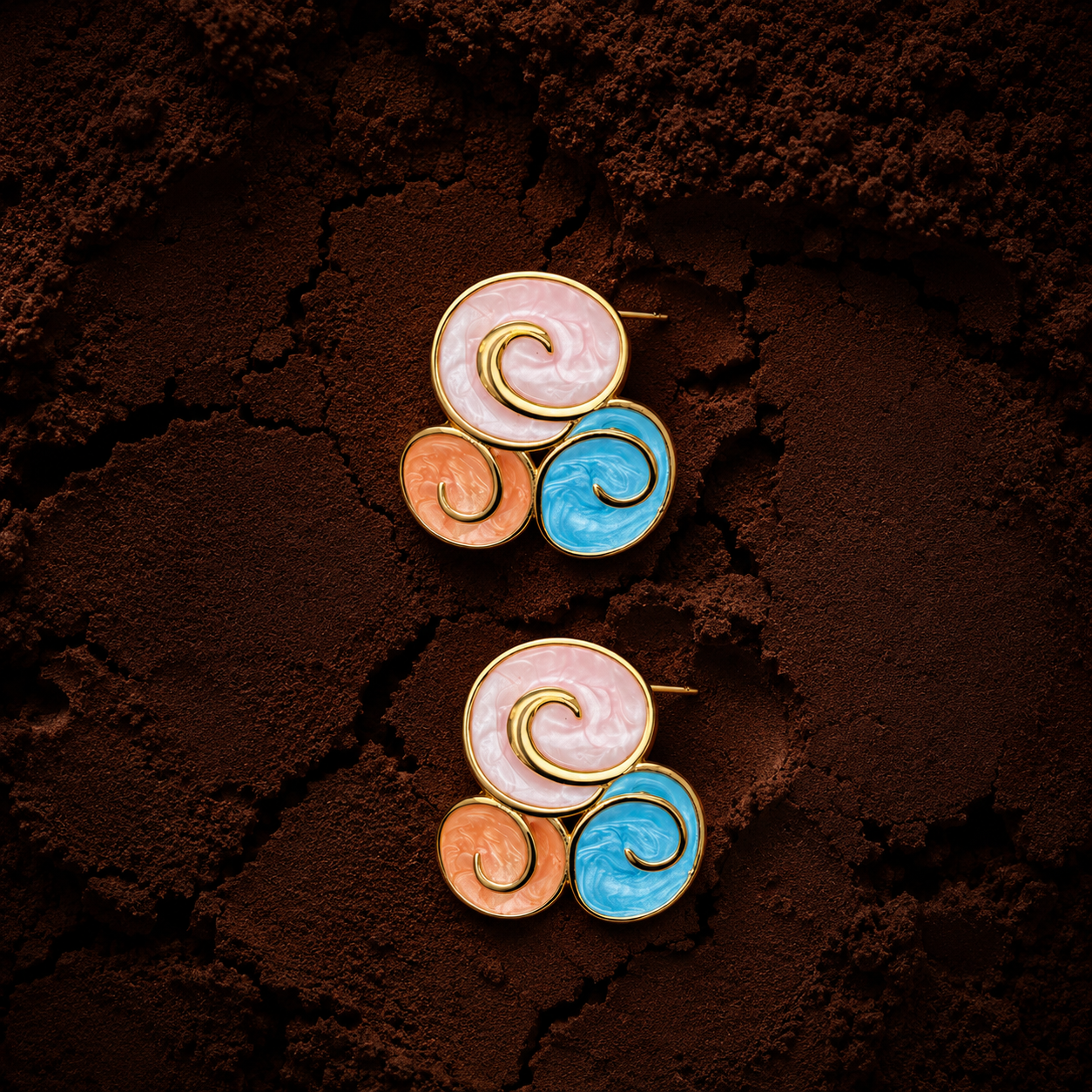Kima Studs colourful enamel swirl stud earrings in pink, coral and blue with gold spiral detail on dark textured background – hypoallergenic statement stud earrings, tarnish-free surgical steel
