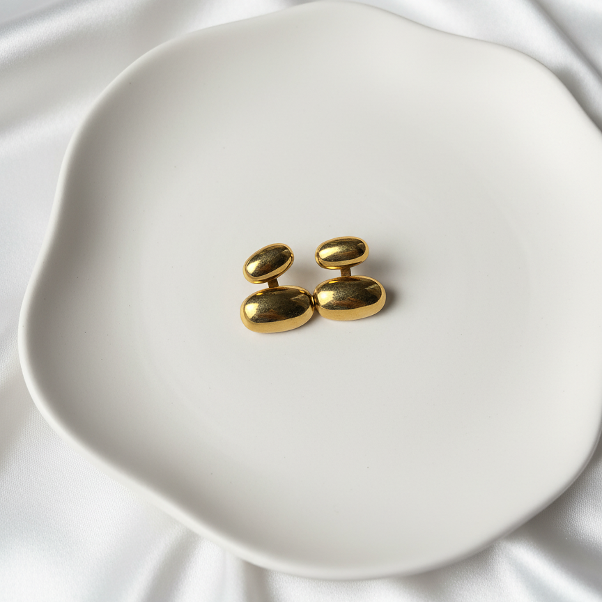 Lea Studs gold stacked bean drop stud earrings on white ceramic dish over silk – minimalist gold and silver earrings, water resistant stainless steel for everyday wear