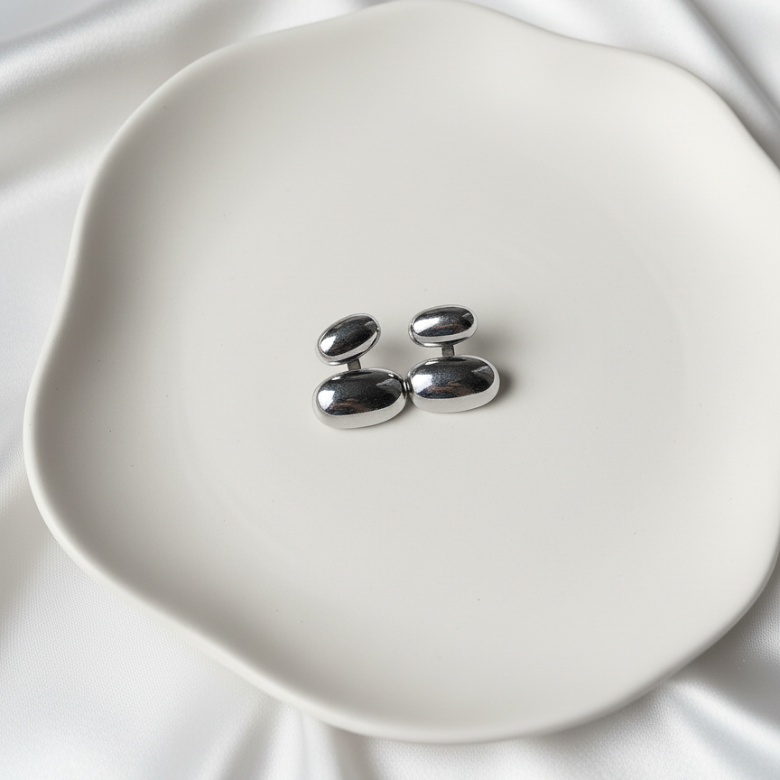 Lea Studs silver stacked bean drop stud earrings on white ceramic dish over silk – minimalist drop stud earrings in hypoallergenic stainless steel that don't tarnish