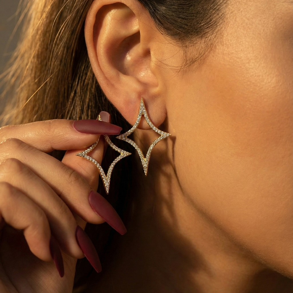 Nova Studs gold sparkle emoji earrings worn on ear with burgundy nails holding second pavé star stud – cubic zirconia statement stud earrings in tarnish free surgical steel