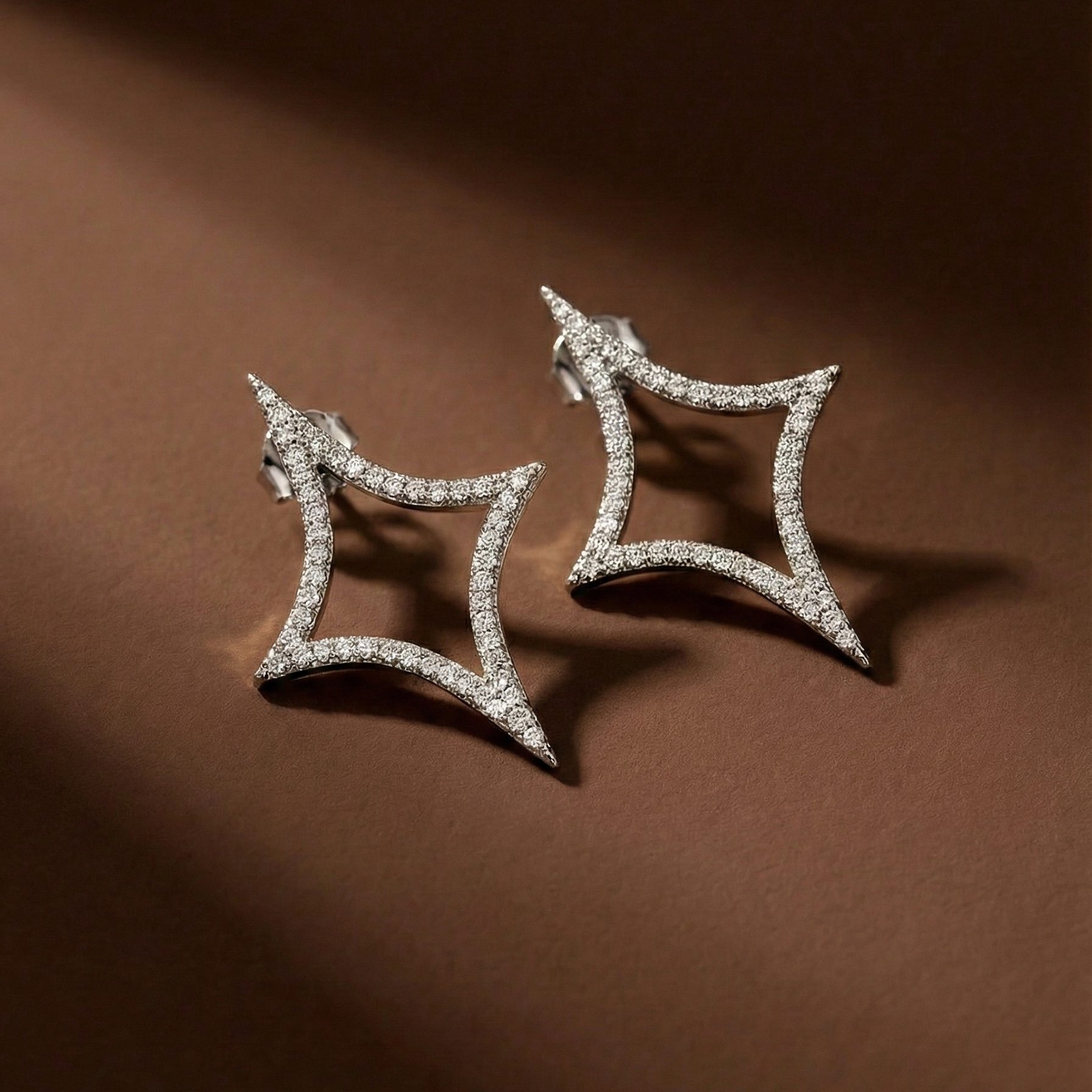 Nova Studs silver pavé star stud earrings flat lay on rich brown background – sparkle emoji cubic zirconia earrings in waterproof surgical steel for sensitive ears