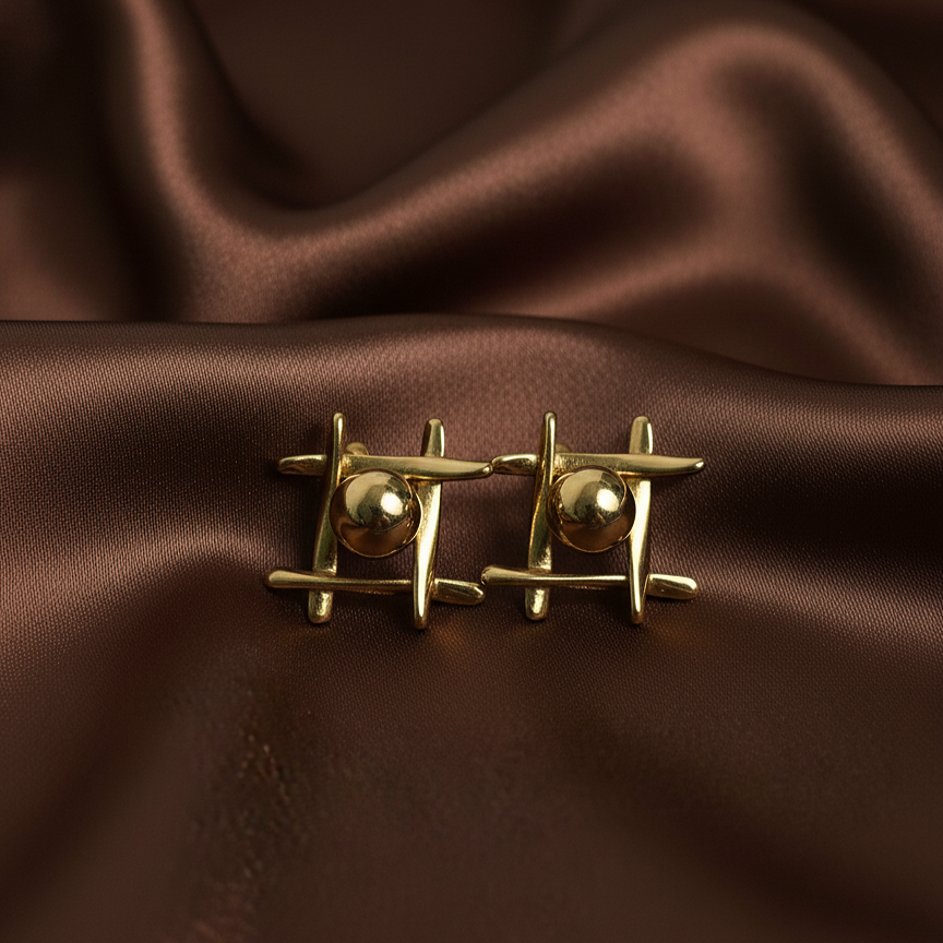 Oma Studs gold geometric bar and ball stud earrings with four intersecting arms and raised sphere centre on dark brown satin – nickel-free tarnish-free waterproof surgical steel stud earrings