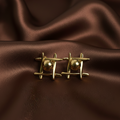 Oma Studs gold geometric bar and ball stud earrings with four intersecting arms and raised sphere centre on dark brown satin – nickel-free tarnish-free waterproof surgical steel stud earrings