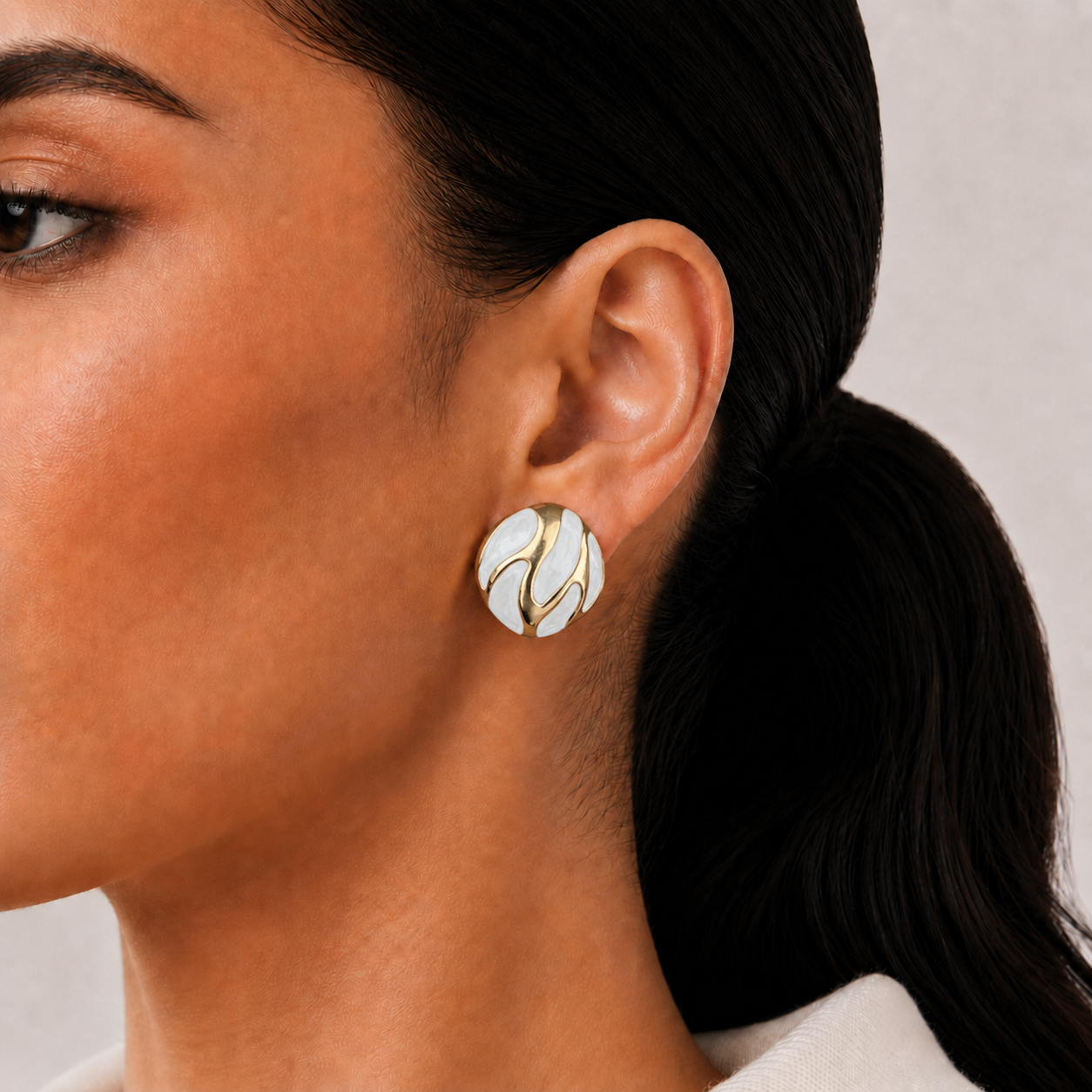 Riva Studs white and gold enamel swirl oval stud earrings with bold wave detail – hypoallergenic nickel-free stainless steel everyday earrings for sensitive ears styled on a lightskinned model 