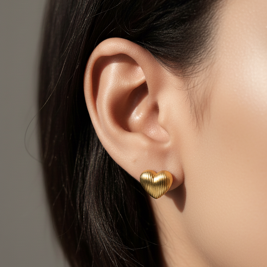 Ugo Studs gold ribbed heart stud earrings worn on ear of model with sleek black hair – minimalist gold studs in hypoallergenic stainless steel for women's everyday wear