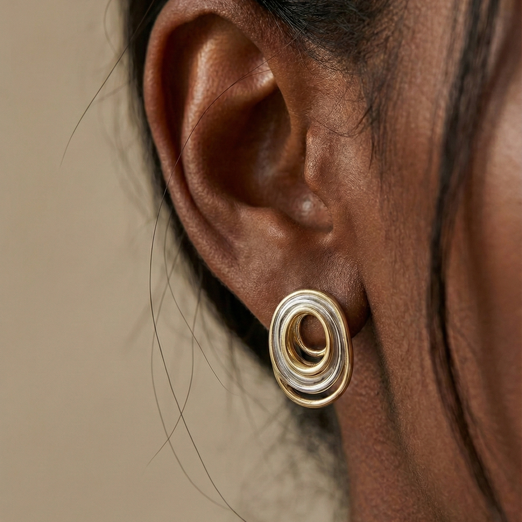 Ùsó Studs gold and silver mixed metal earring worn on ear in editorial close-up – flat back hypoallergenic spiral oval stud earrings in modern two tone stainless steel