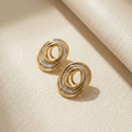 Ùsó Studs gold and silver mixed metal earrings on cream leather background – two tone spiral oval stud earrings in waterproof stainless steel that don't tarnish for modern wear