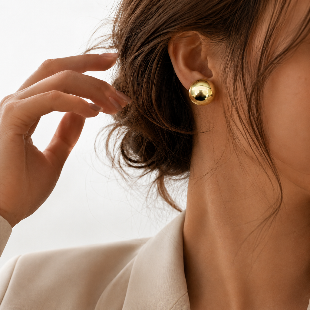 Xena Studs gold polished dome stud earring worn on ear of brunette model in cream blazer – hypoallergenic stainless steel stud earrings, tarnish free best everyday earrings