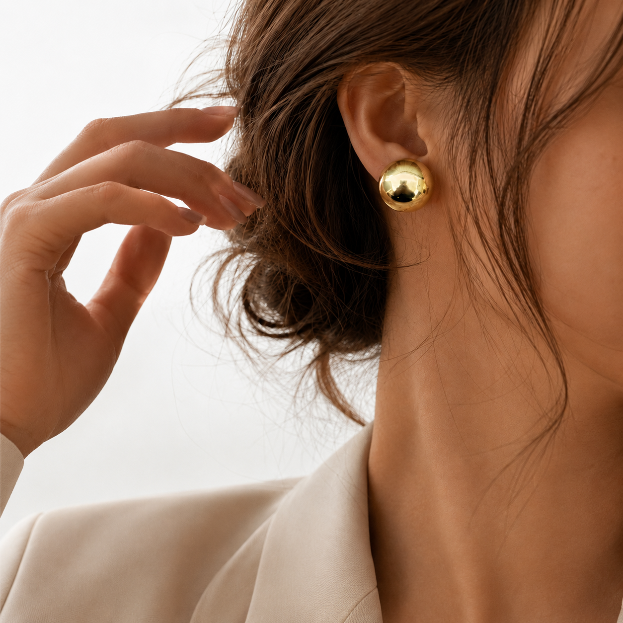 Xena Studs gold polished dome stud earring worn on ear of brunette model in cream blazer – hypoallergenic stainless steel stud earrings, tarnish free best everyday earrings